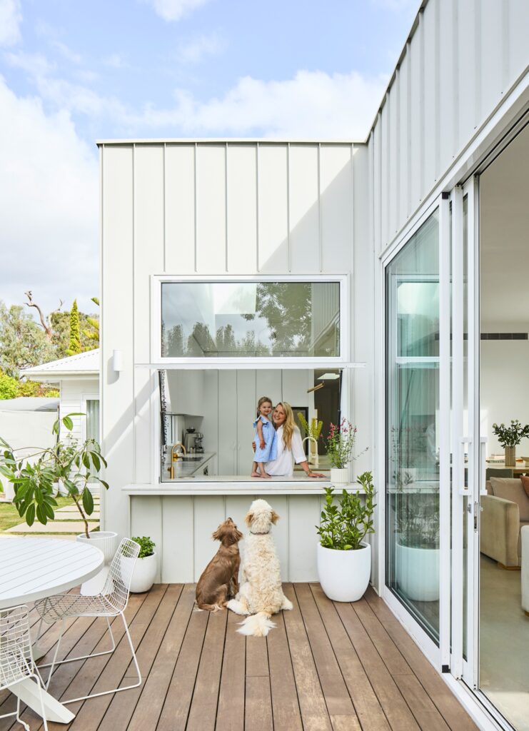 two dogs on a timber deck looking up at a kitchen servery window